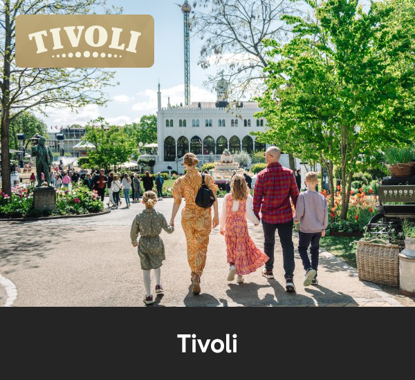 Familj som promenerar i Tivoli med blomsterplanteringar och nöjesparkens byggnader i bakgrunden