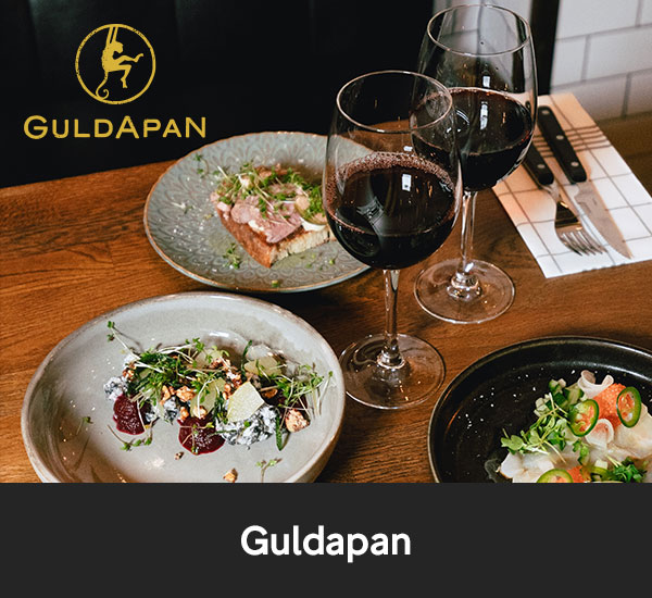 Tre tallrikar med nordiska smårätter och två glas rött vin på ett träbord på restaurang Guldapan i Karlstad