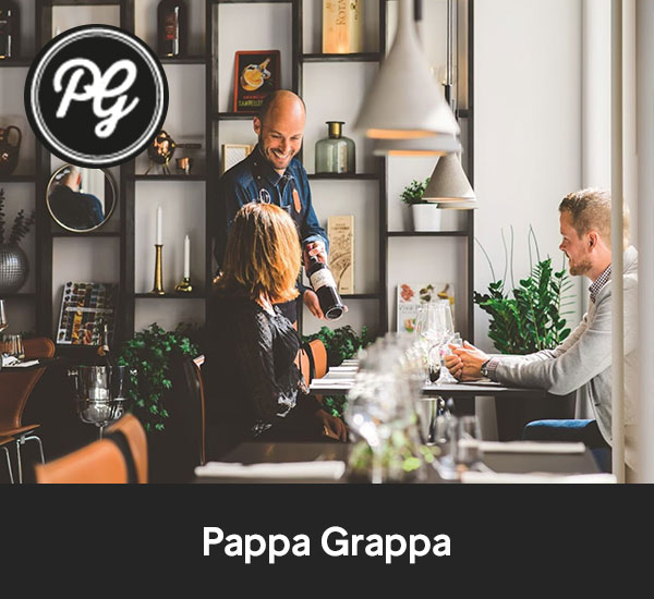 Servitör serverar vin till två gäster vid ett bord på restaurang Pappa Grappa